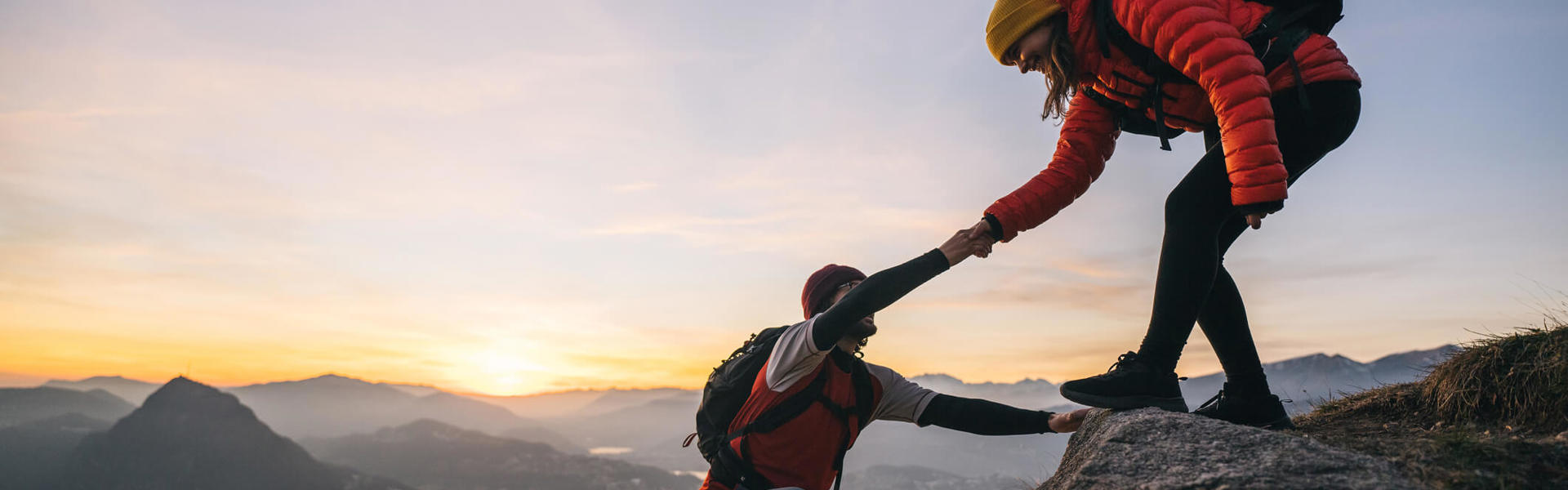 a person stood at the top of a mountain helping another person up to the summit