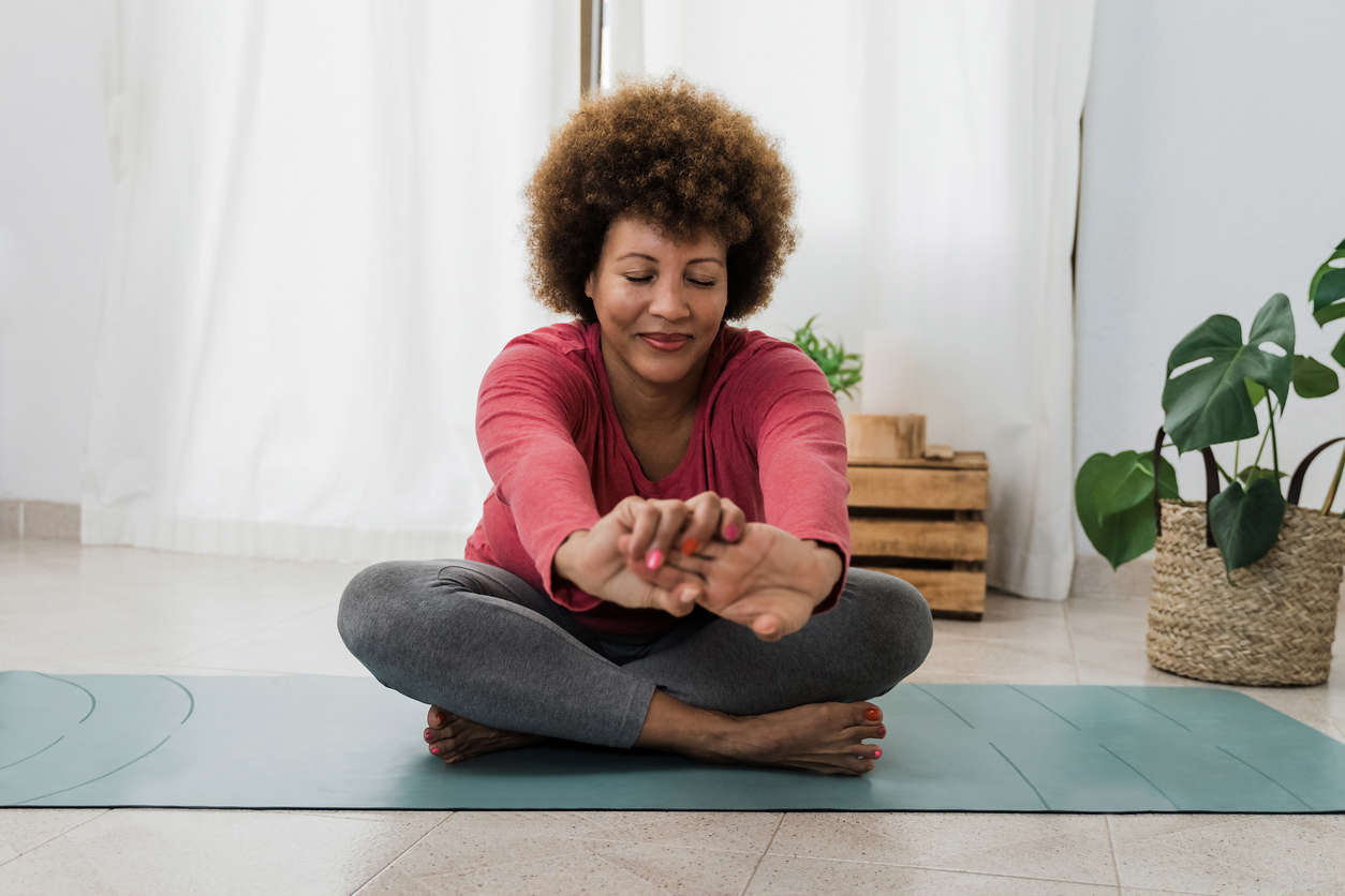 A woman sat on a green yoga mat cross legged and stretching her hands forward