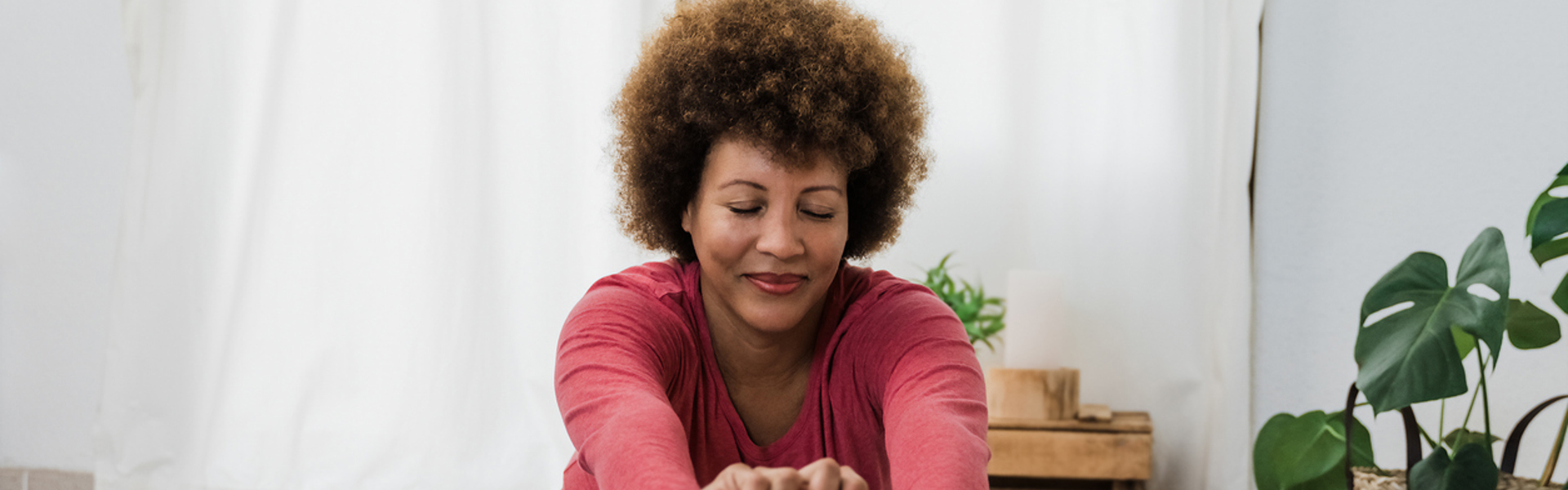 A woman sat on a green yoga mat cross legged and stretching her hands forward