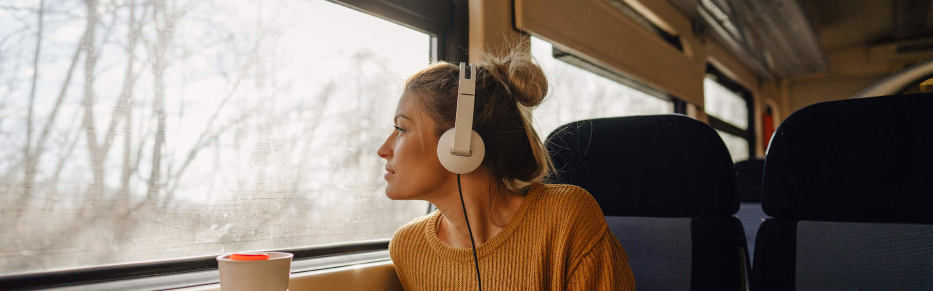 a woman wearing a yellow jumper wearing headphones on a train looking out of the window