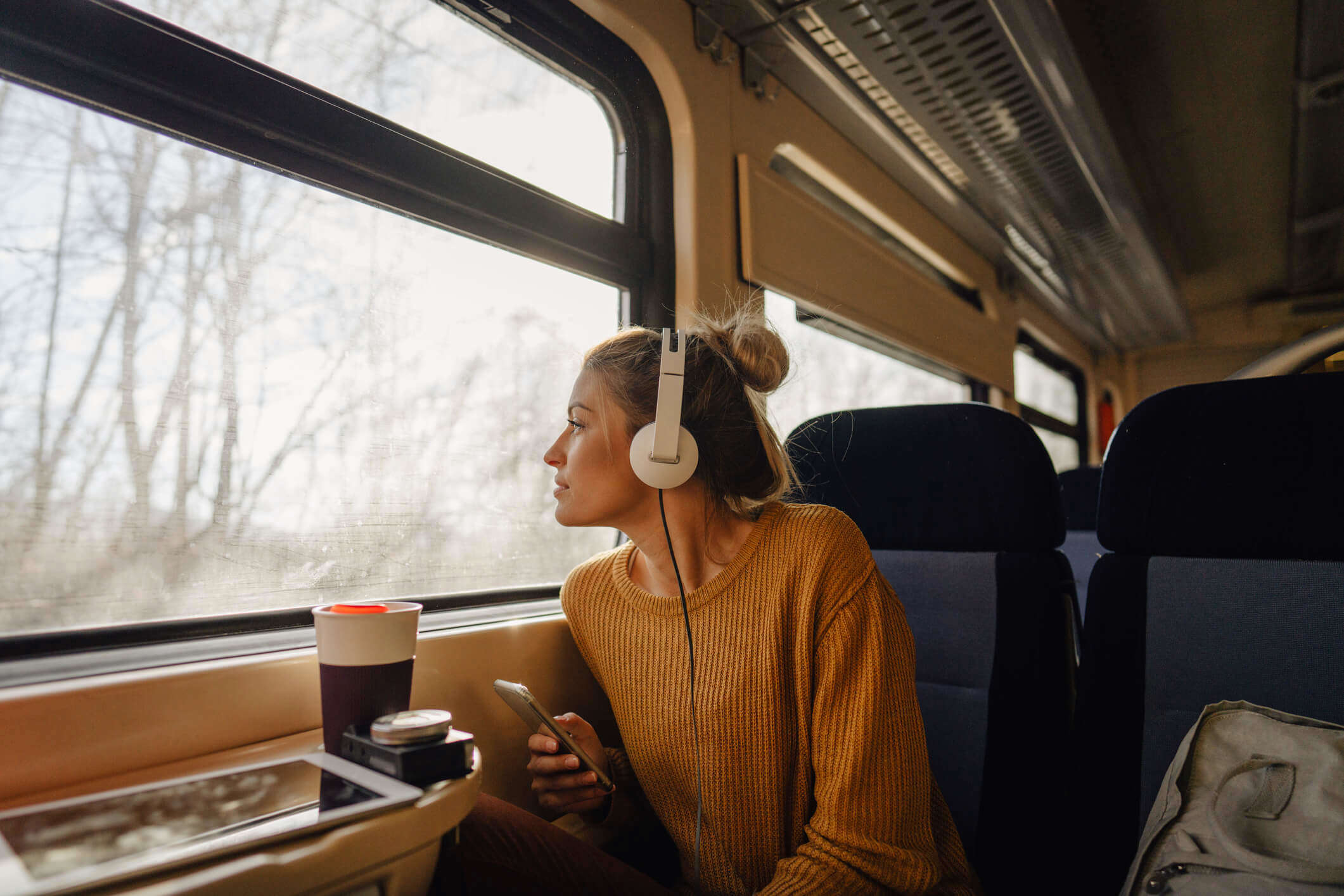 a woman wearing a yellow jumper wearing headphones on a train looking out of the window