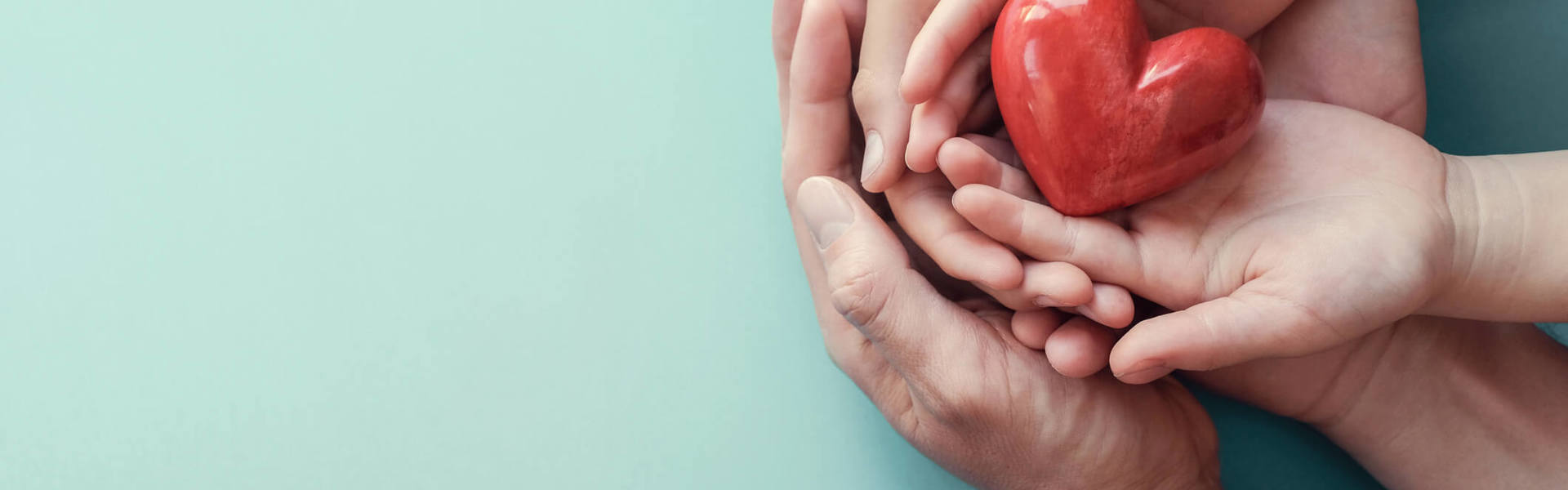 a parent and child's hands both holding a red heart ornament