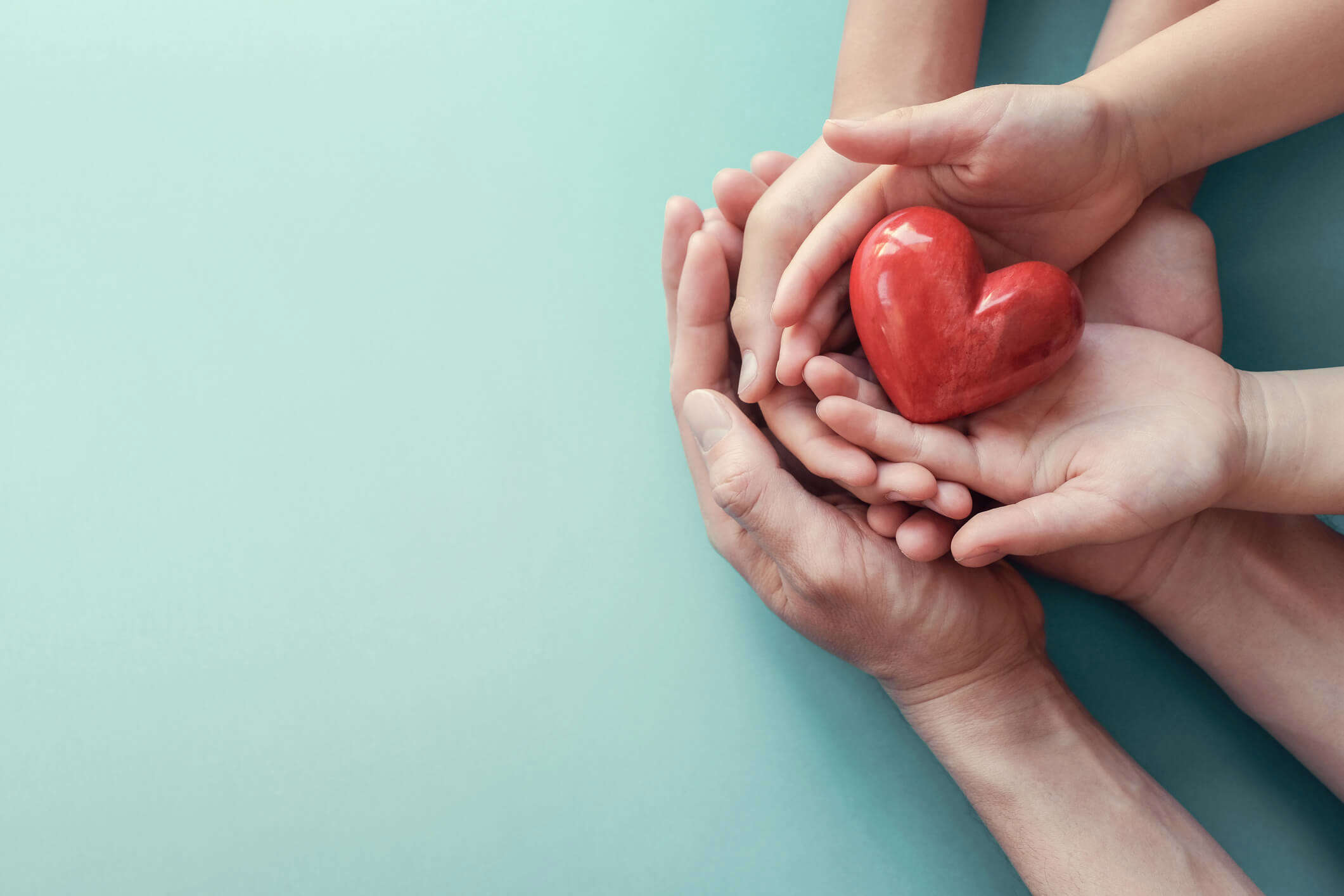 a parent and child's hands both holding a red heart ornament