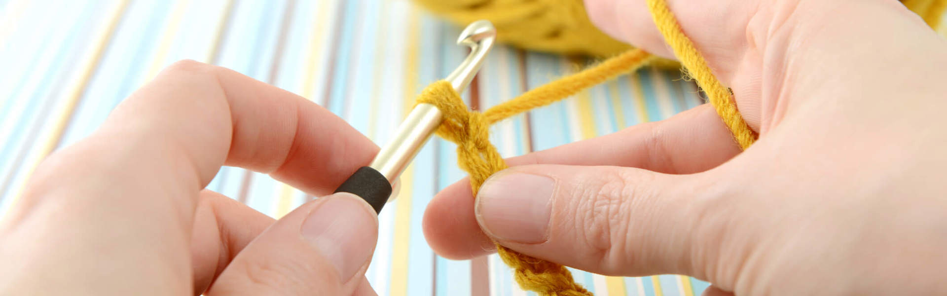 a person crocheting with a crochet hook and yellow yarn