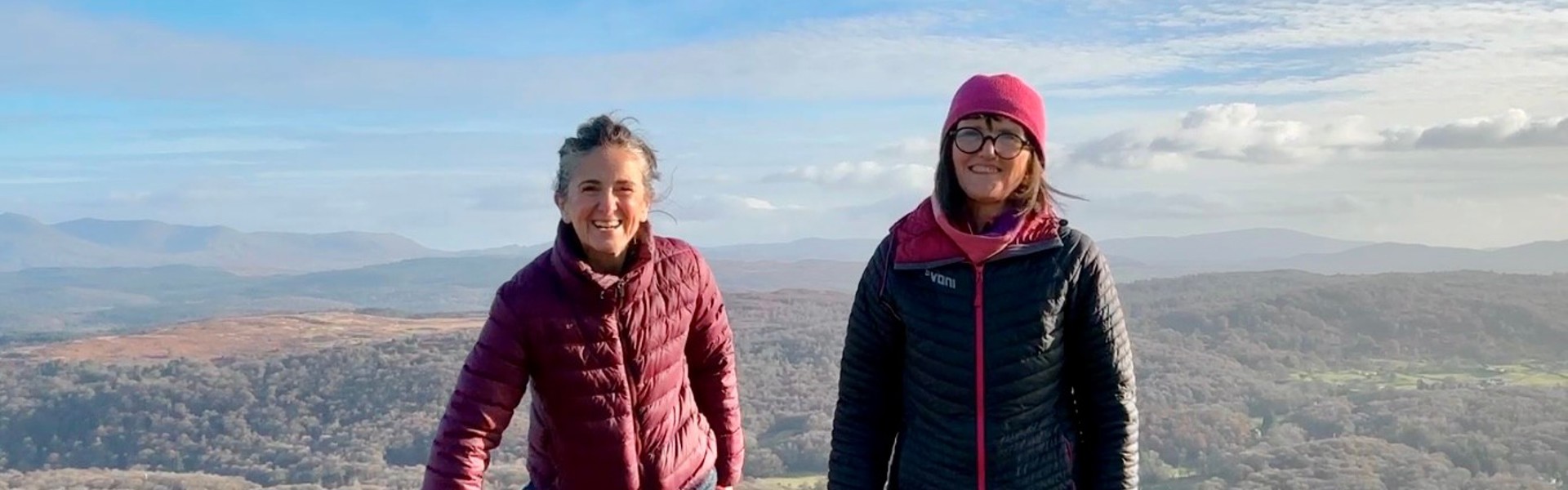 Elaine Fisher (right) and Jo Andrews (left) with Willow the black spaniel, stood on a hill with a beautiful background of the Lake District.