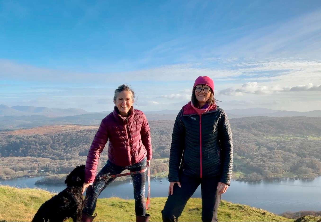 Elaine Fisher (right) and Jo Andrews (left) with Willow the black spaniel, stood on a hill with a beautiful background of the Lake District.