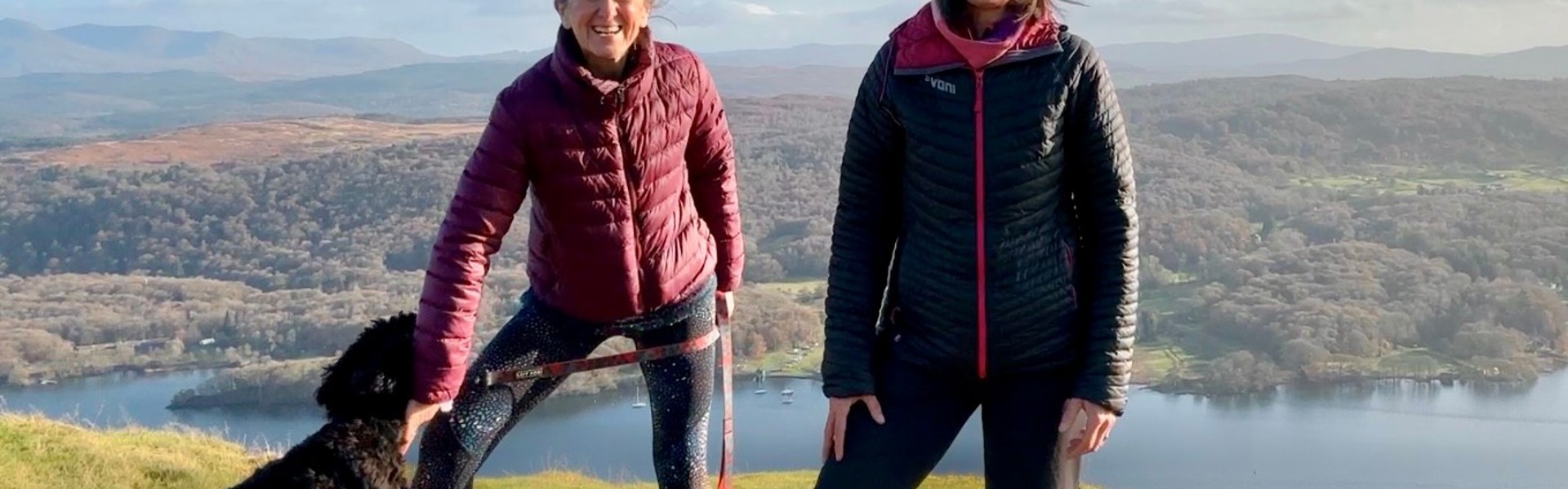 Elaine Fisher (right) and Jo Andrews (left) with Willow the black spaniel, stood on a hill with a beautiful background of the Lake District.