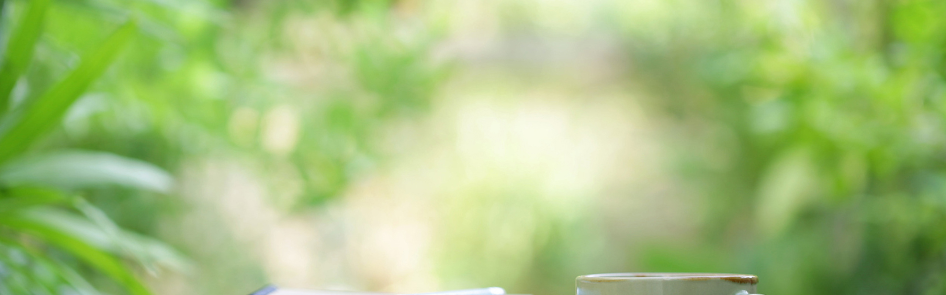 a pile of writing books with a blue pencil resting on top on a wooden table with a green outdoor background