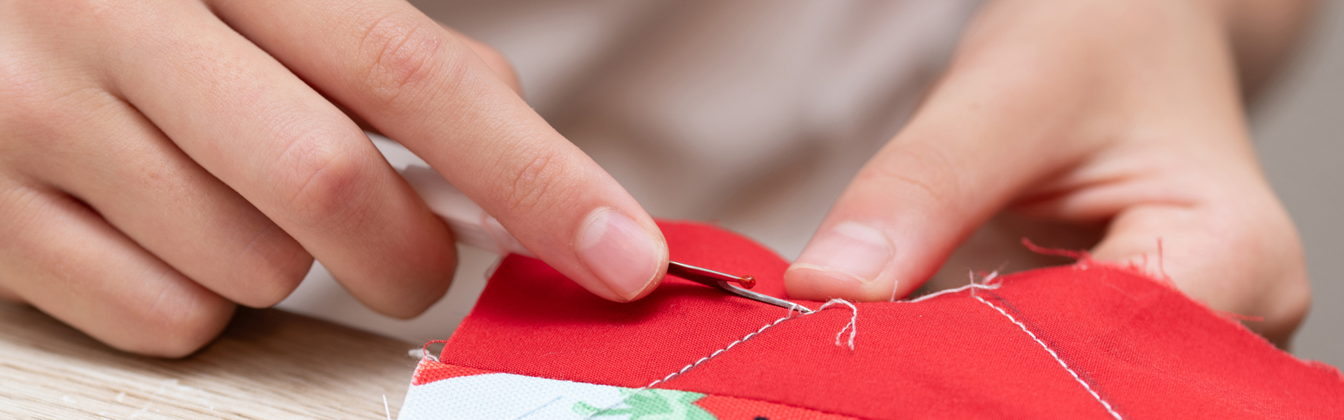 Main image: a close-up image of a woman sewing on a strawberry printed fabric.
