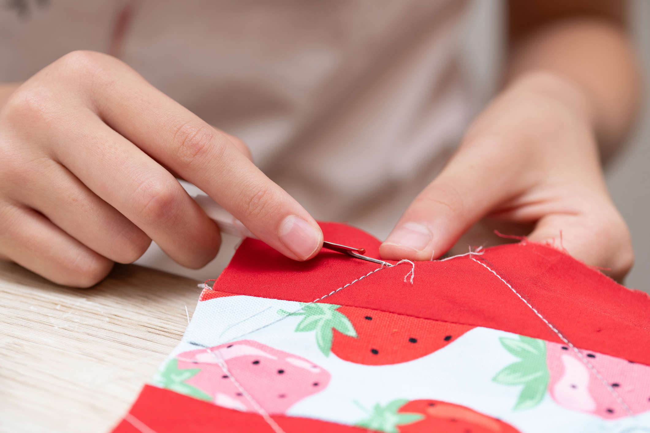 Main image: a close-up image of a woman sewing on a strawberry printed fabric.