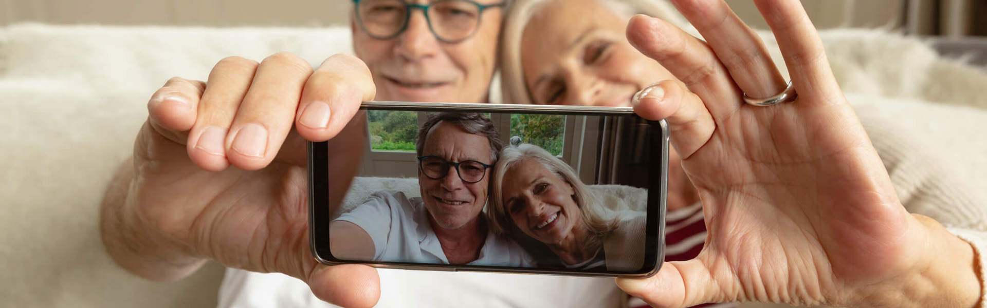 an older couple sat on a sofa taking a selfie