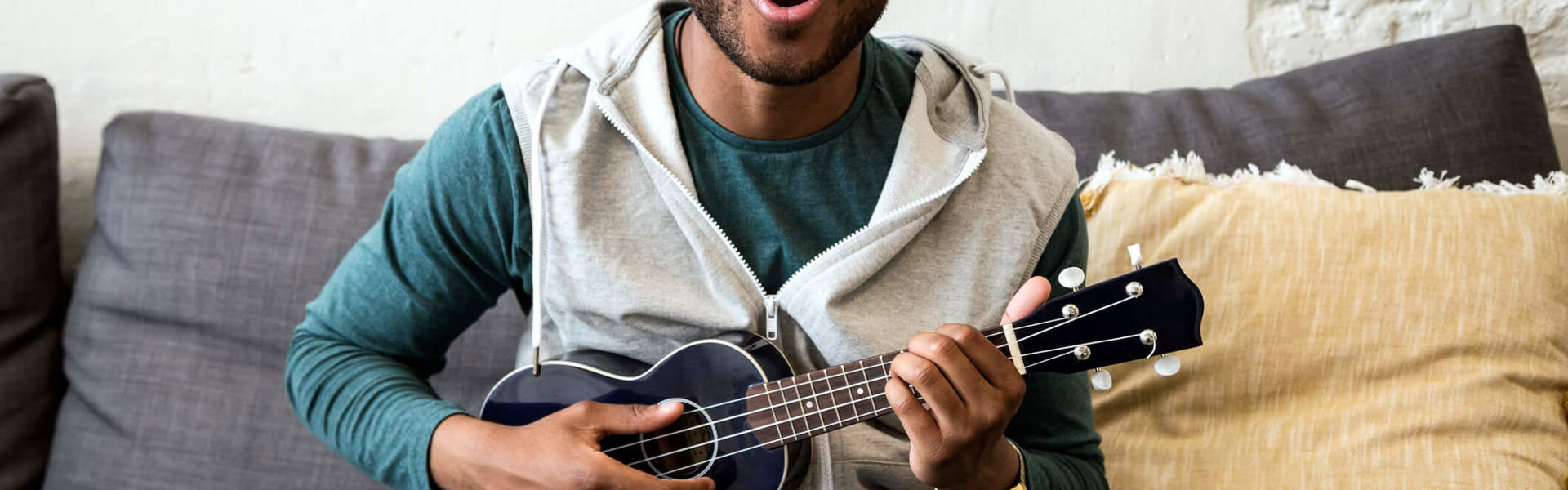 a man wearing glasses sat on the sofa playing the ukulele and singing