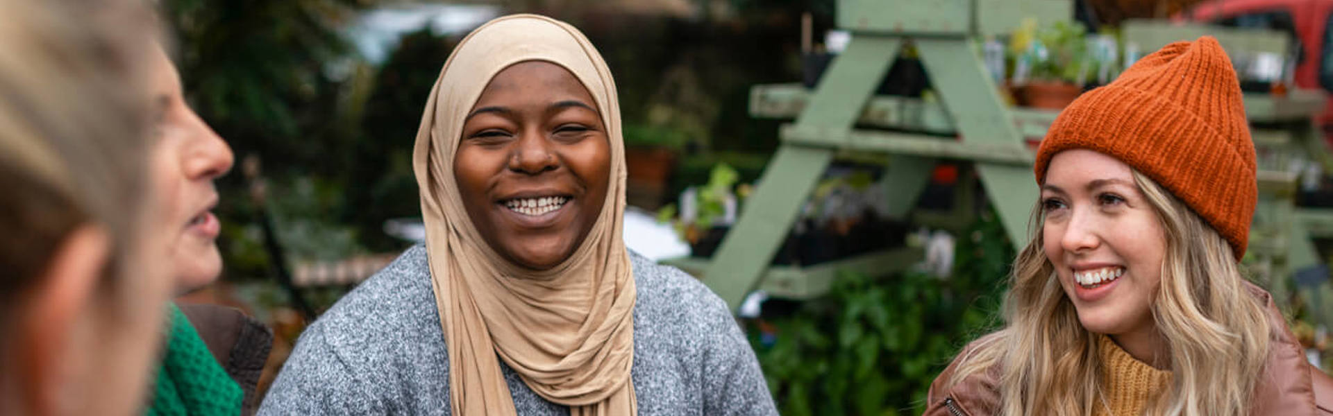 Volunteers sitting outdoors wearing warm casual clothing on a sunny cold winters day. They are resting and having a tea break from working on a community farm, looking after crops and performing other sustainable and environmentally friendly tasks. They are laughing and talking together, drinking hot drinks.