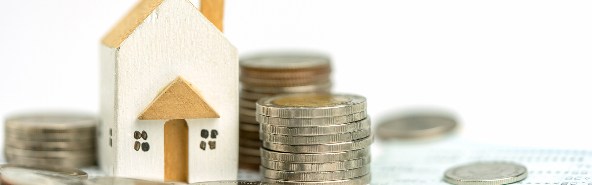 A little white and brown/yellow wooden house sculpture, sitting next to stacks of coins