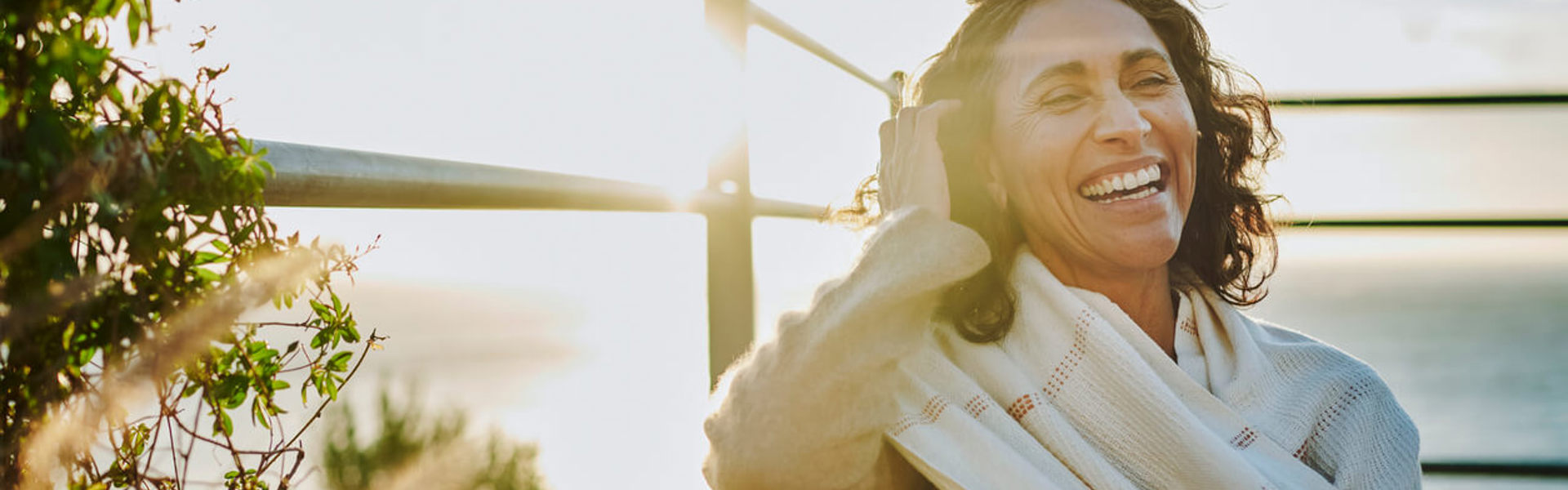 a woman wearing a scarf sat on a balcony laughing and pulling her hair away from her face