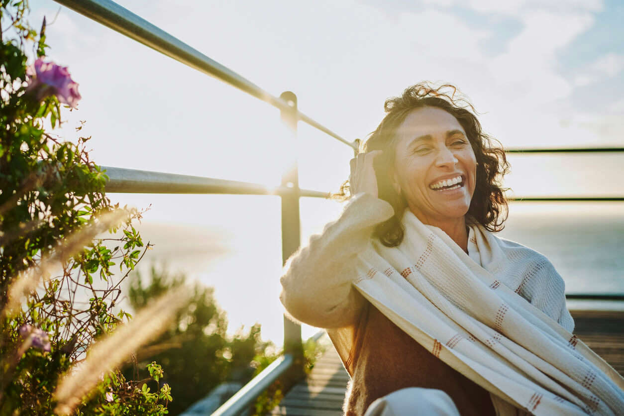 a woman wearing a scarf sat on a balcony laughing and pulling her hair away from her face