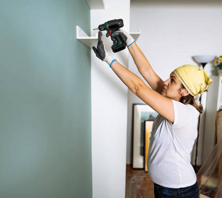 a woman putting up a DIY shelf at home using a drill