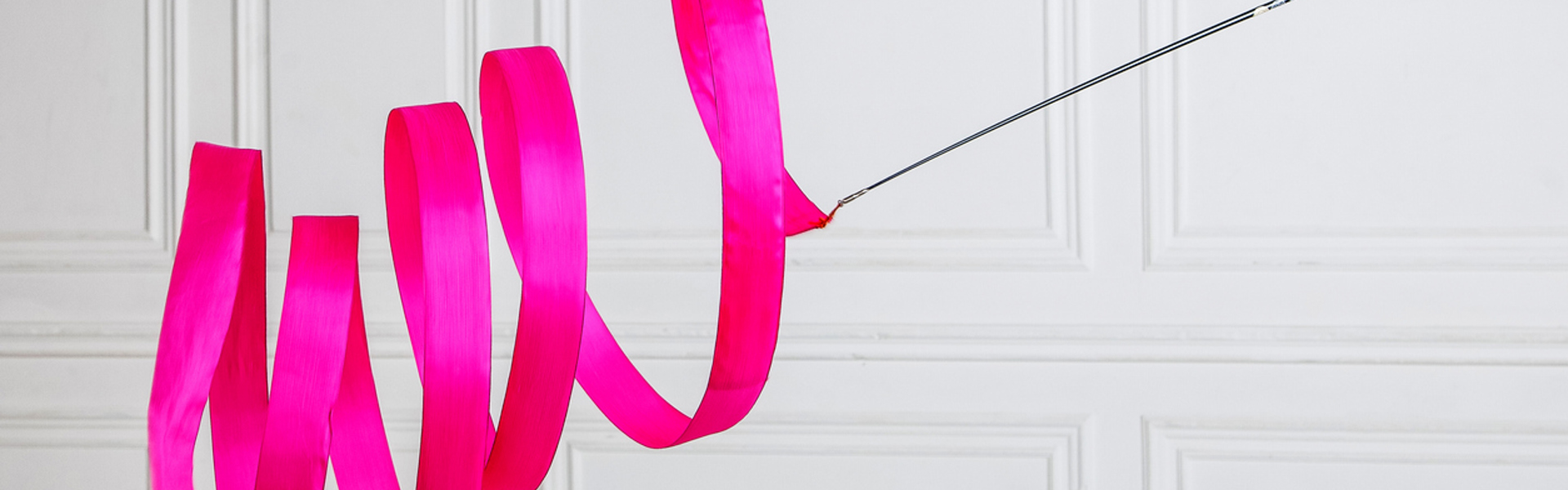 a pink rhythmic gymnastics ribbon against a white wall