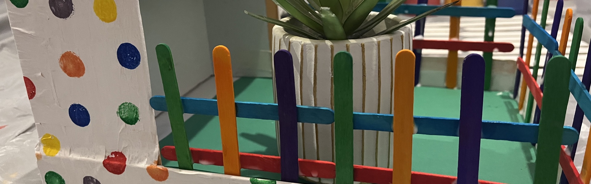 Main Image: photo of a dementia-friendly craft - indoor allotment. The card board is painted white with multi-coloured spots - with a succulent plant in the middle.