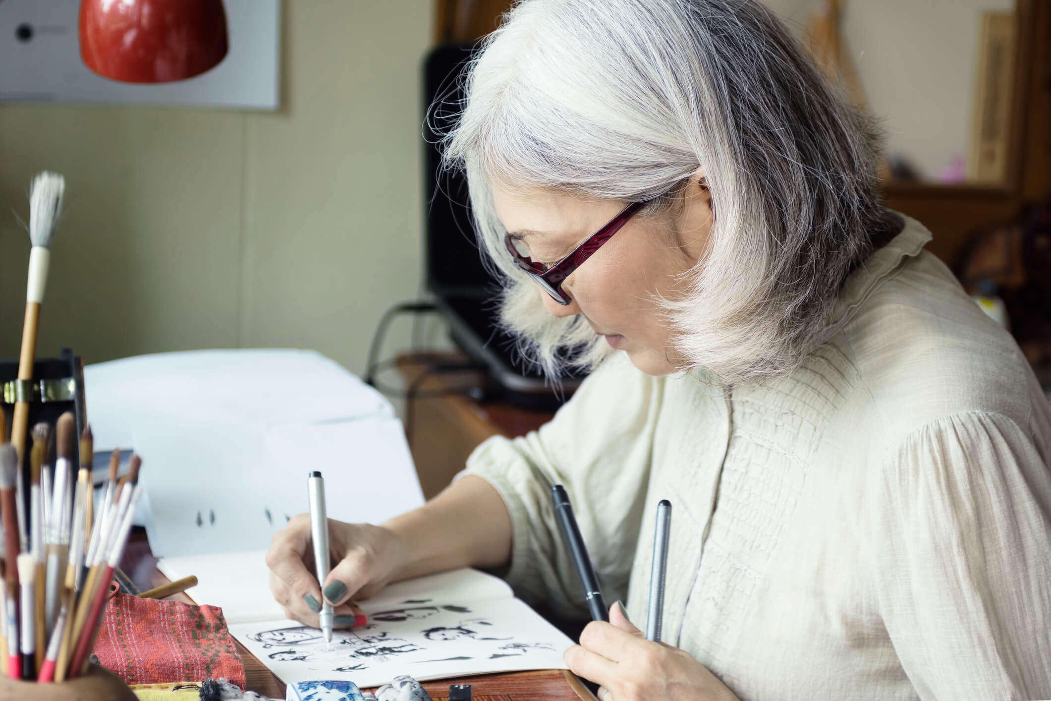 an older woman sat at a desk sketching