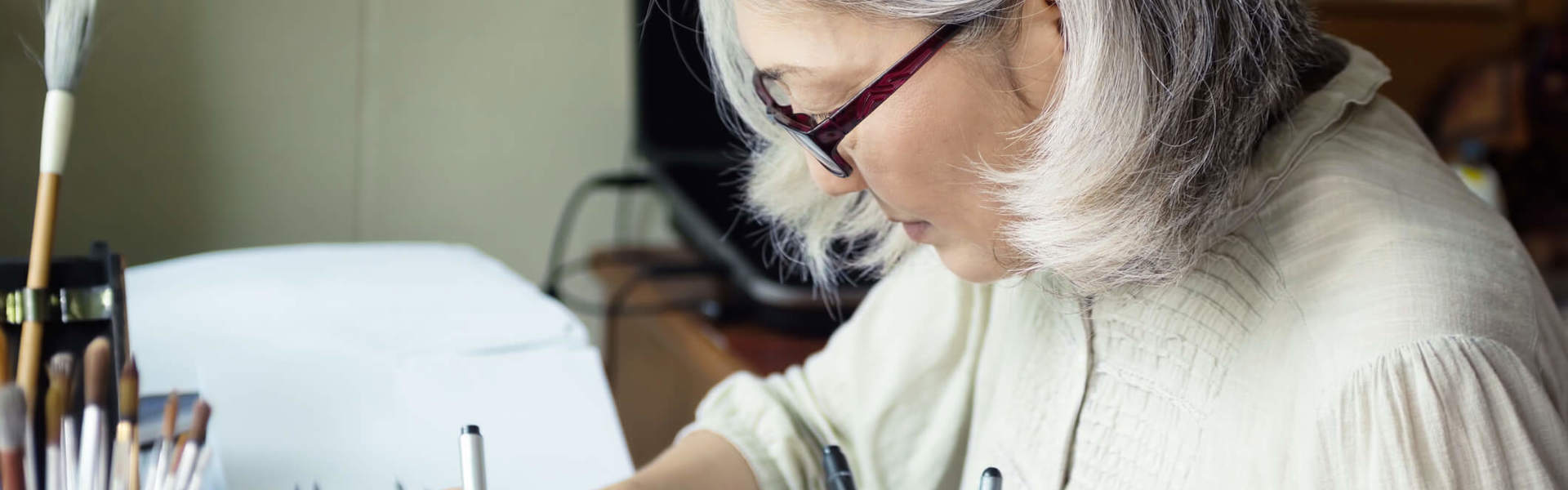 an older woman sat at a desk sketching