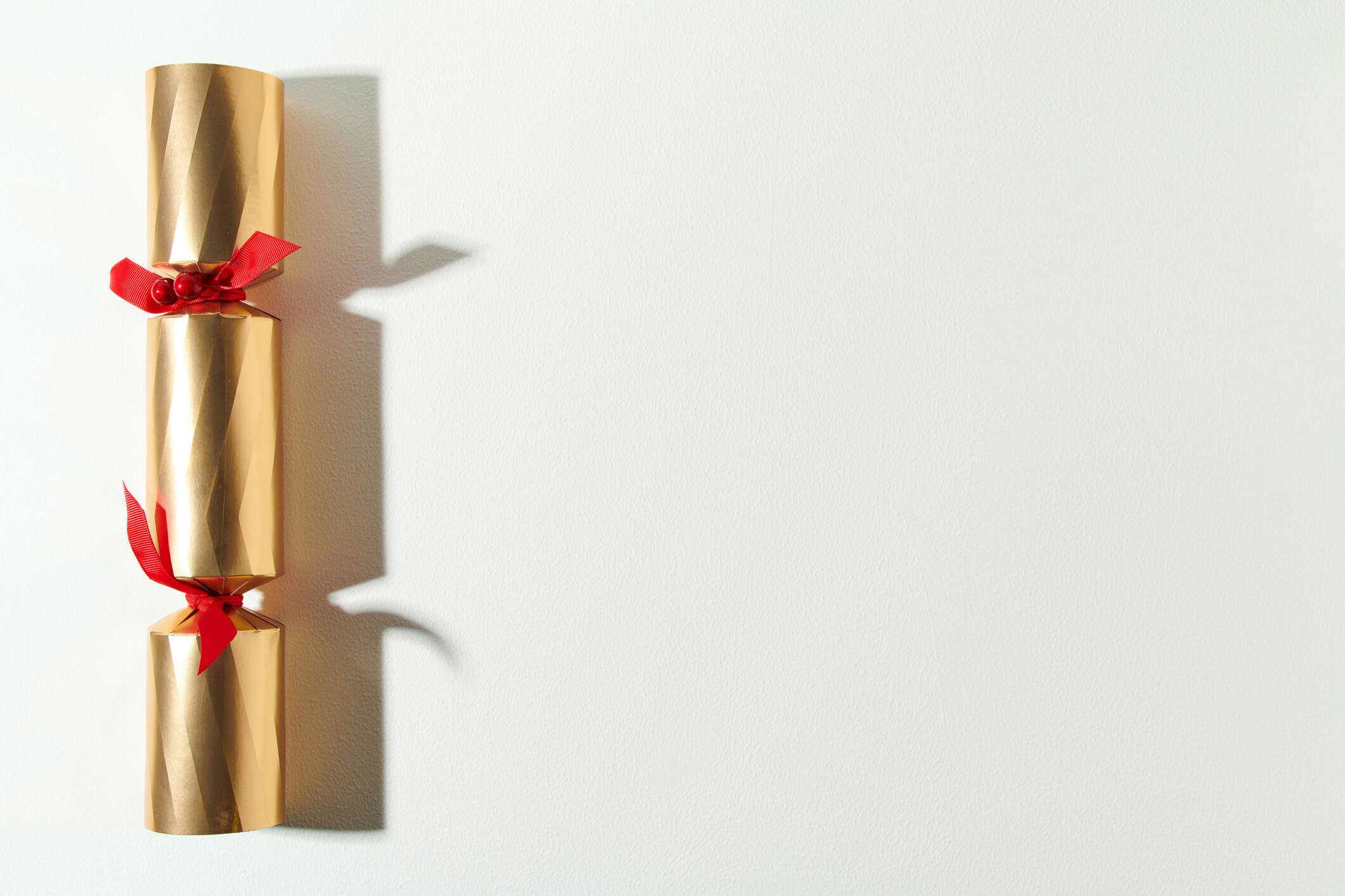 a gold Christmas cracker with red ribbon bows on a white background