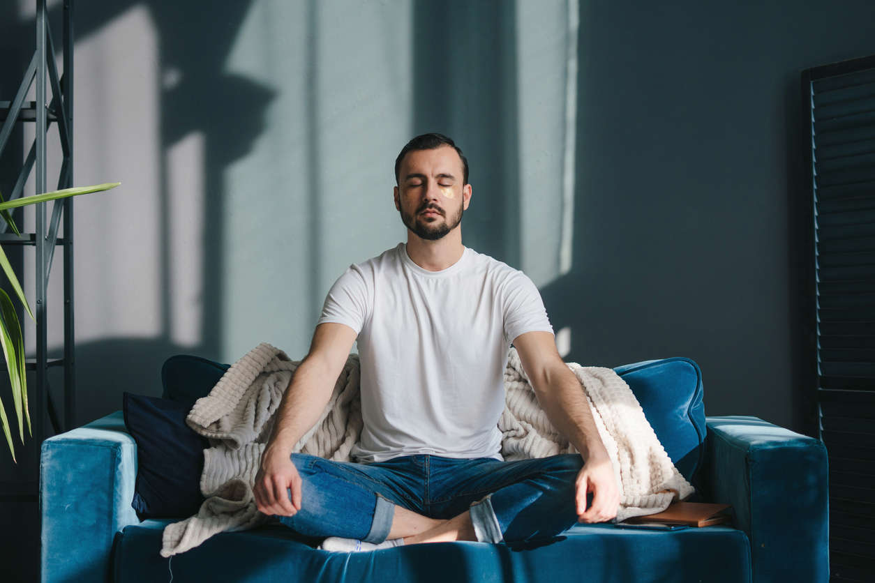 a man sat cross legged on a sofa at home meditating