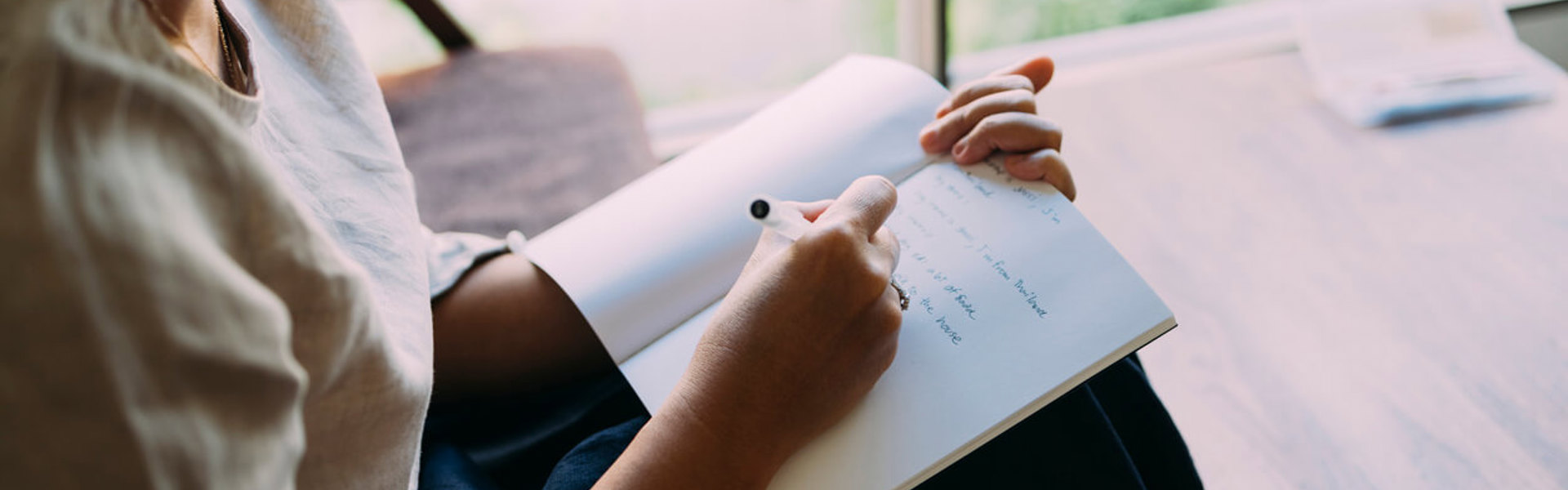 Anonymous woman sitting in her living room, writing in her notebook.