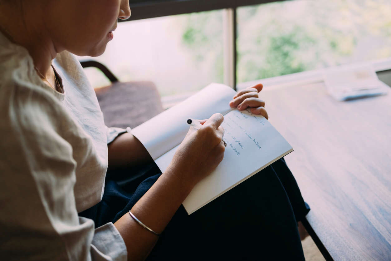 Anonymous woman sitting in her living room, writing in her notebook.