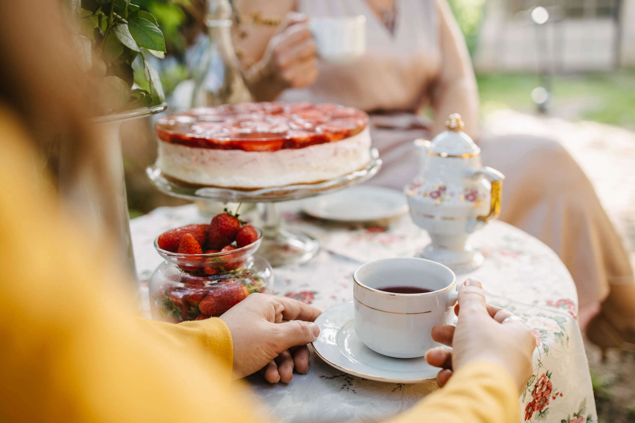 a traditional English afternoon tea table spread with a teacup and saucer, a strawberry cake and pot of fresh strawberries