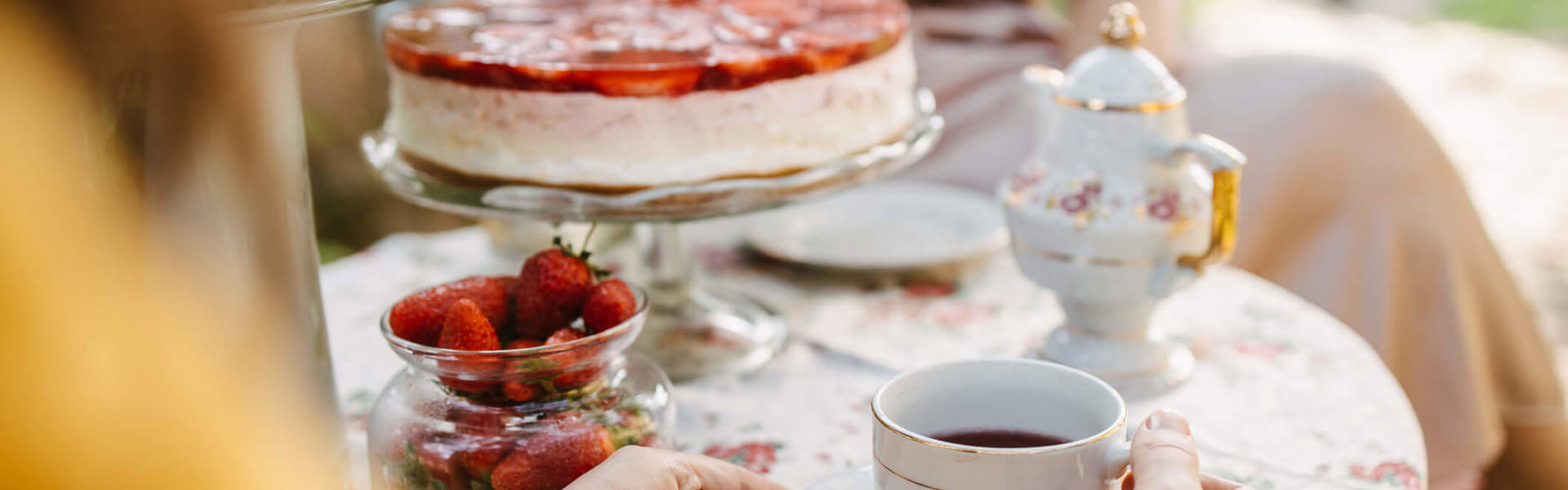 a traditional English afternoon tea table spread with a teacup and saucer, a strawberry cake and pot of fresh strawberries