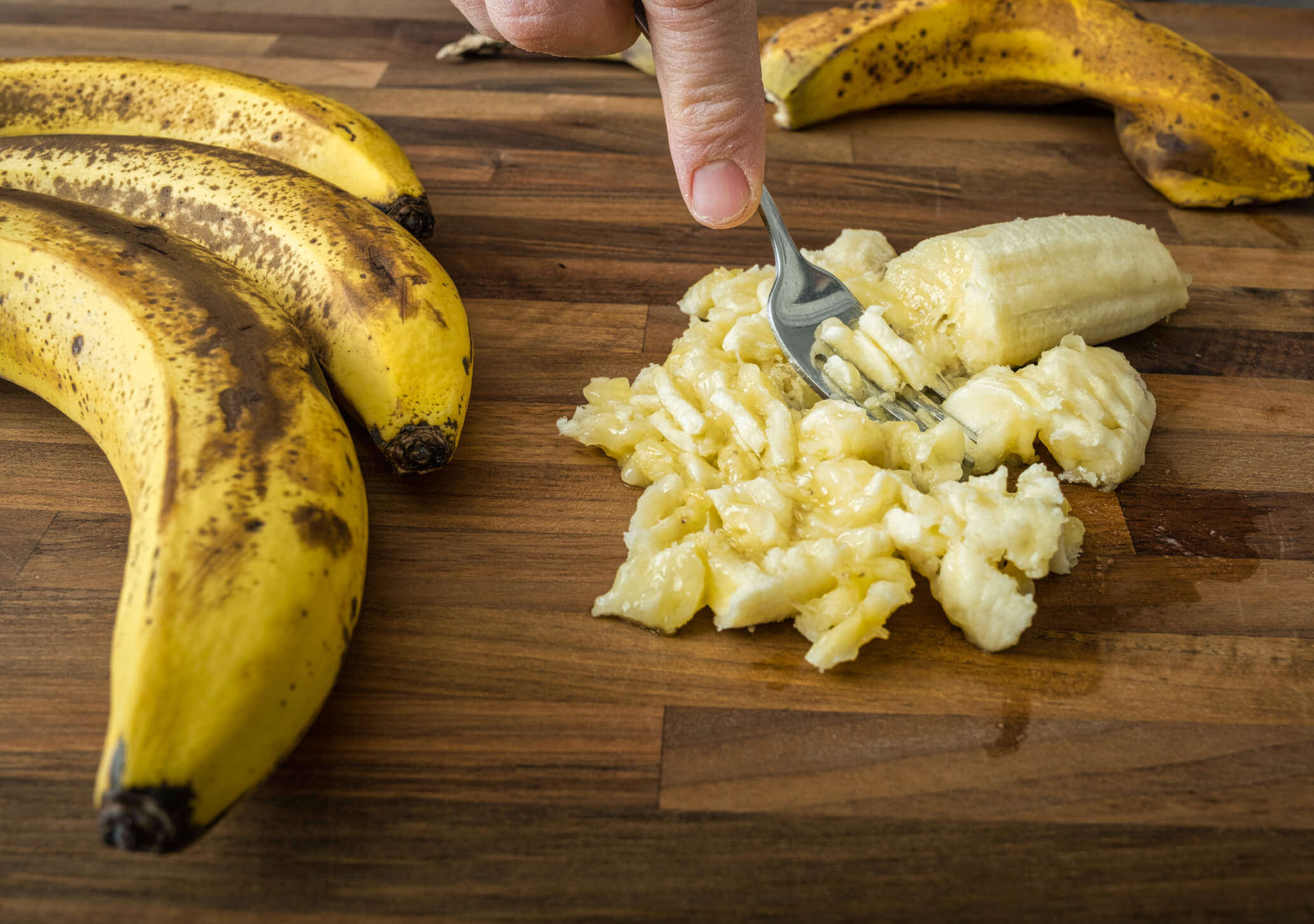 someone mashing banana up on a wooden chopping board next to a bunch of bananas