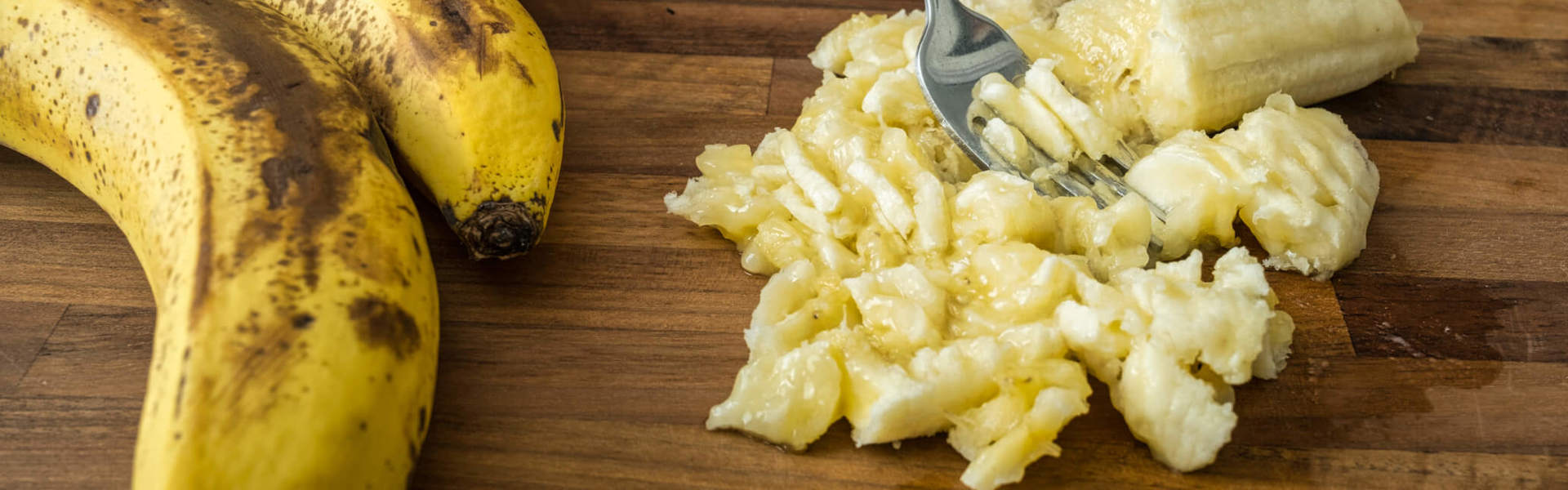 someone mashing banana up on a wooden chopping board next to a bunch of bananas