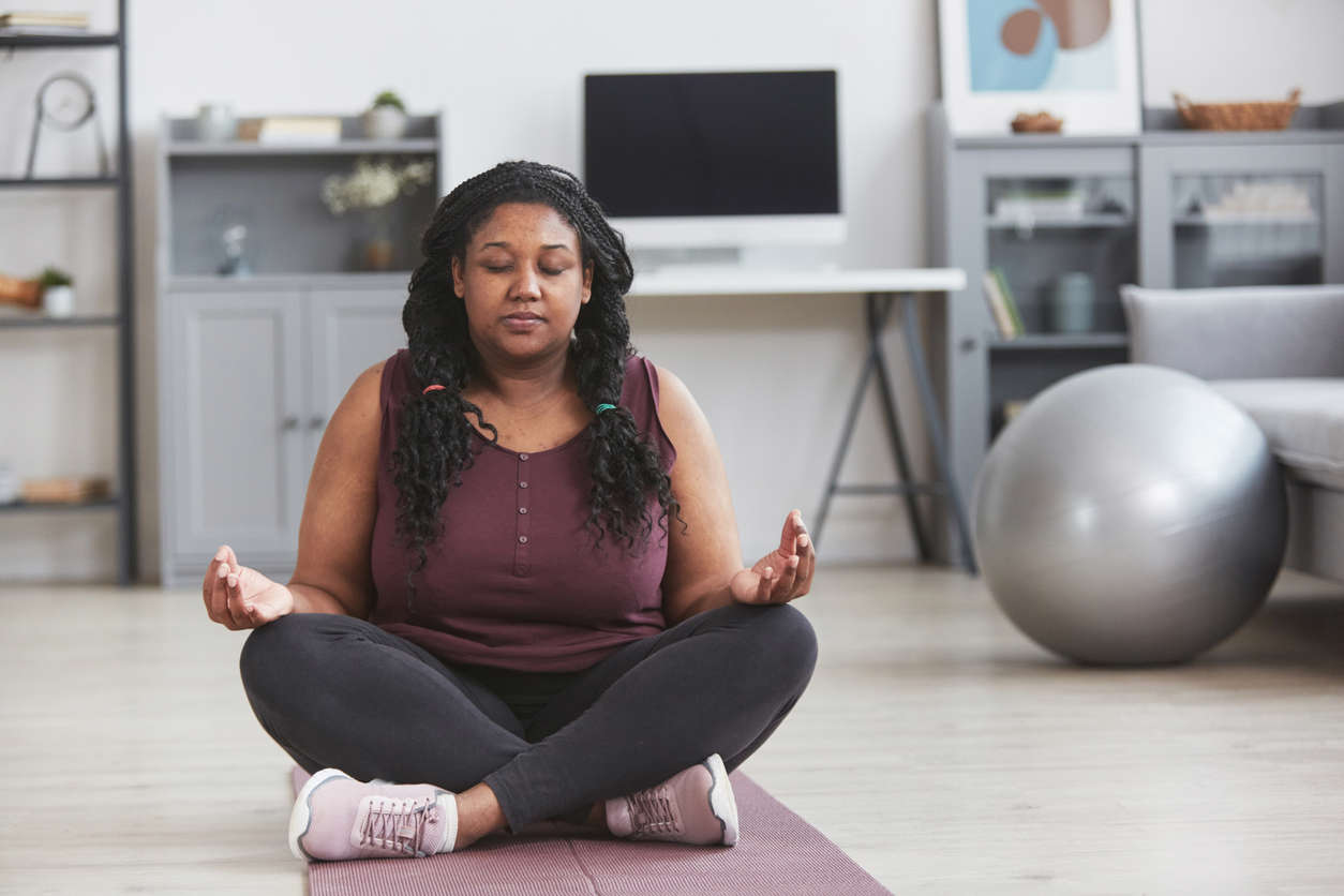 a woman sat cross legged with eyes closed in the living room meditating at home