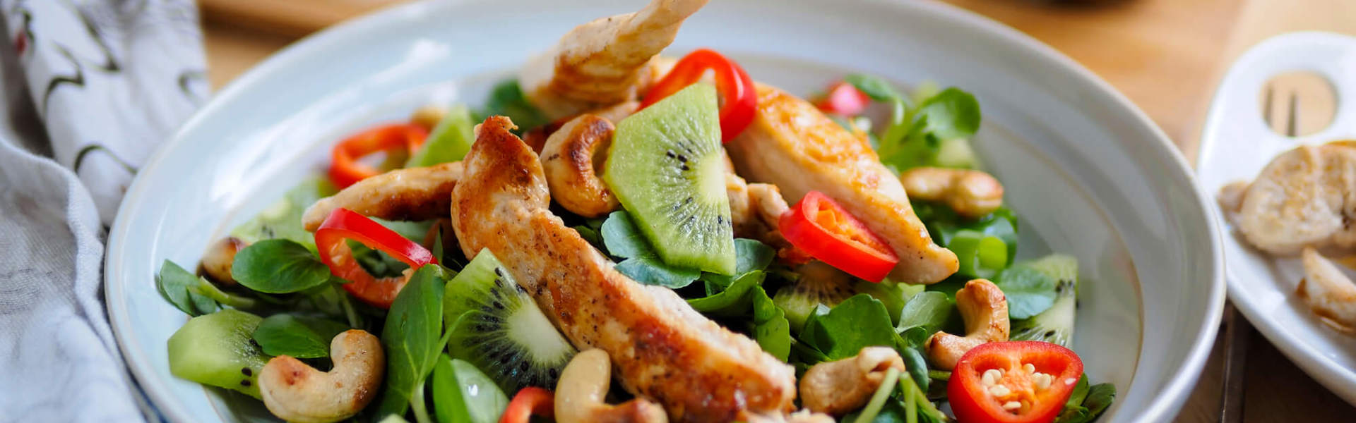 A chilli and ginger chicken in a white bowl with kiwi fruit spring onions and cashews