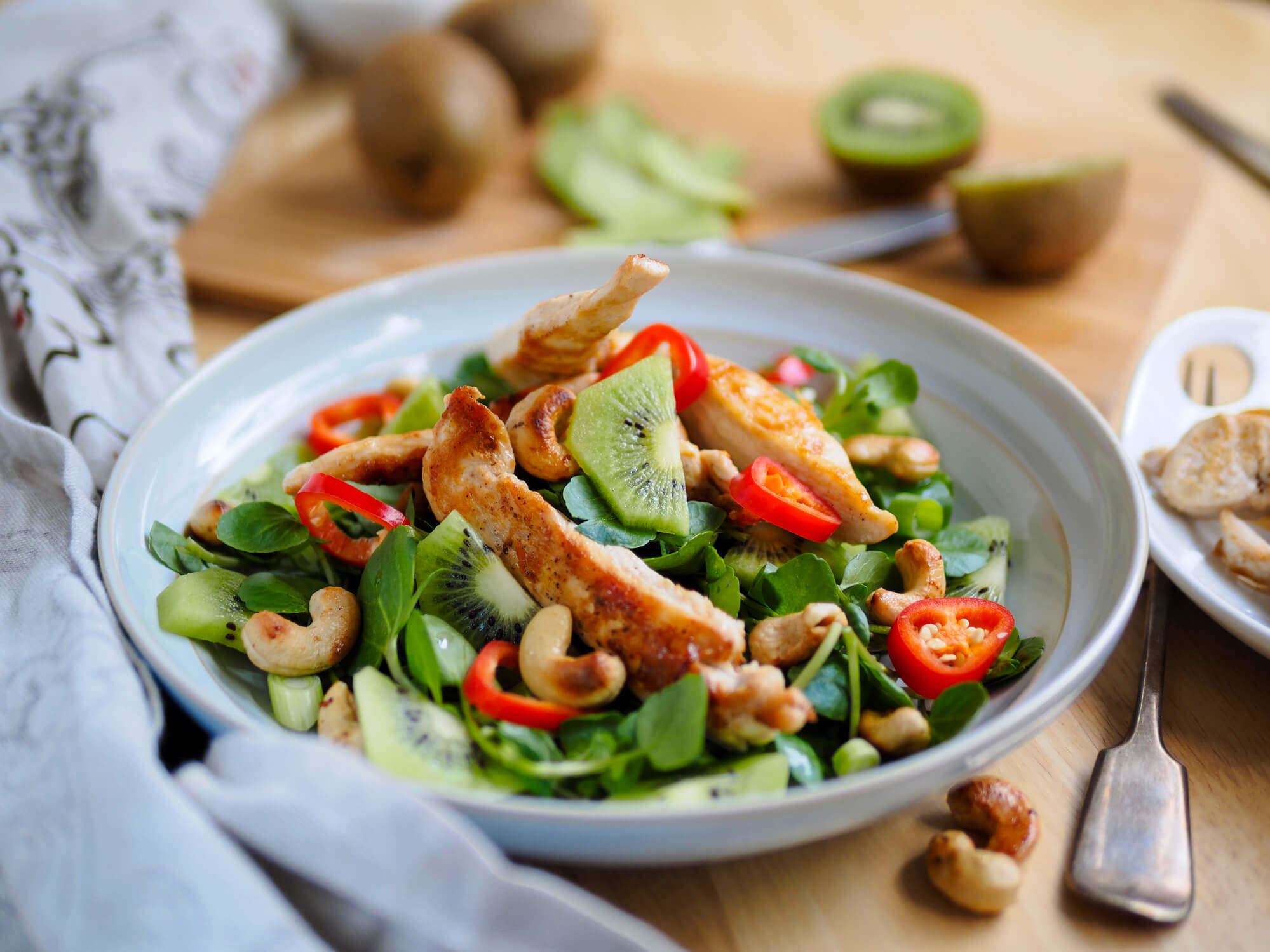 A chilli and ginger chicken in a white bowl with kiwi fruit spring onions and cashews