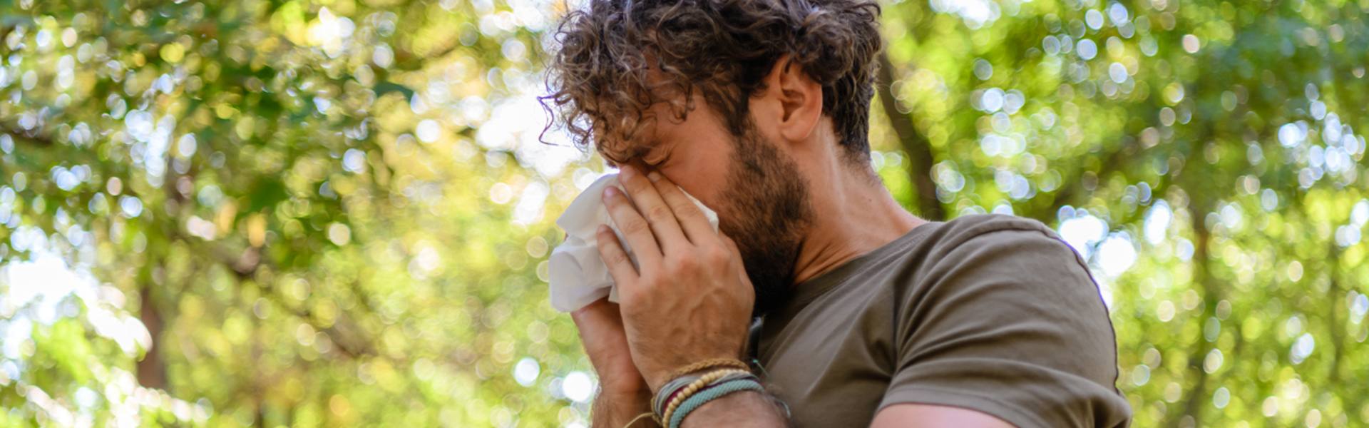 a man sneezing into a tissue whilst outdoors