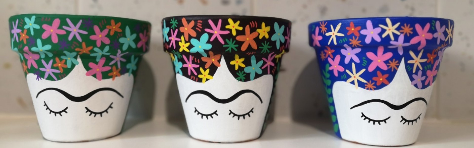 Painted ceramic plant pots in a variety of colours depicting a painted image of Frida Kahlo's face with eyes closed