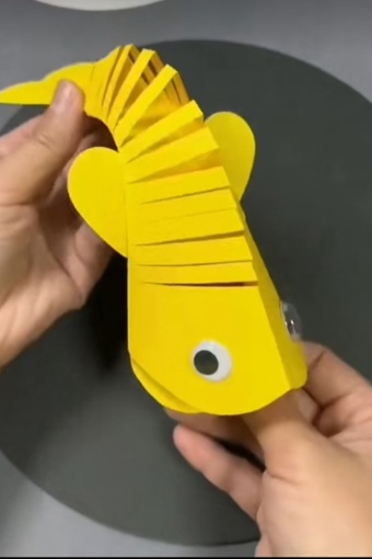 Main Image: A yellow paper folding fish with googly eyes, craft for kids.