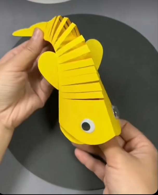 Main Image: A yellow paper folding fish with googly eyes, craft for kids.