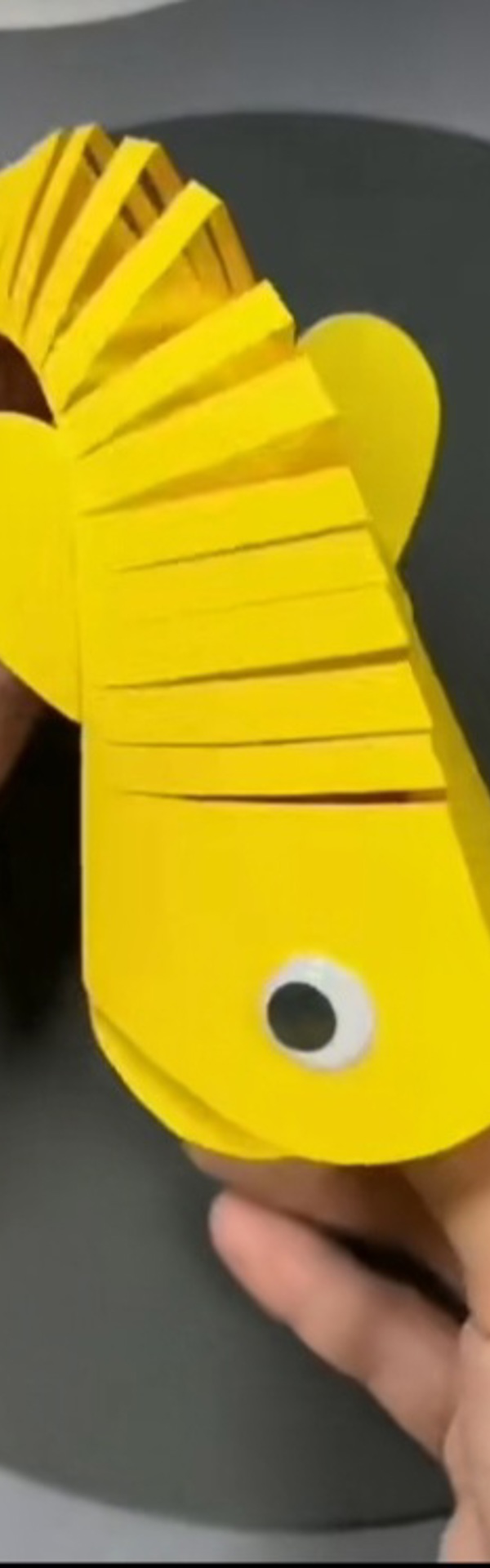 Main Image: A yellow paper folding fish with googly eyes, craft for kids.