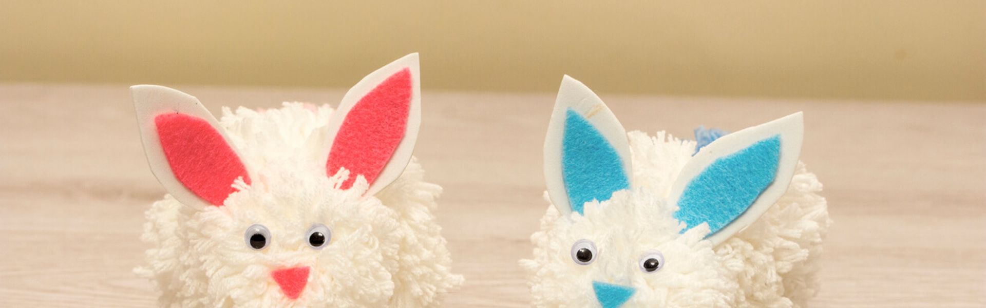 white pompom bunnies with blue and pink felt ears on a wooden table
