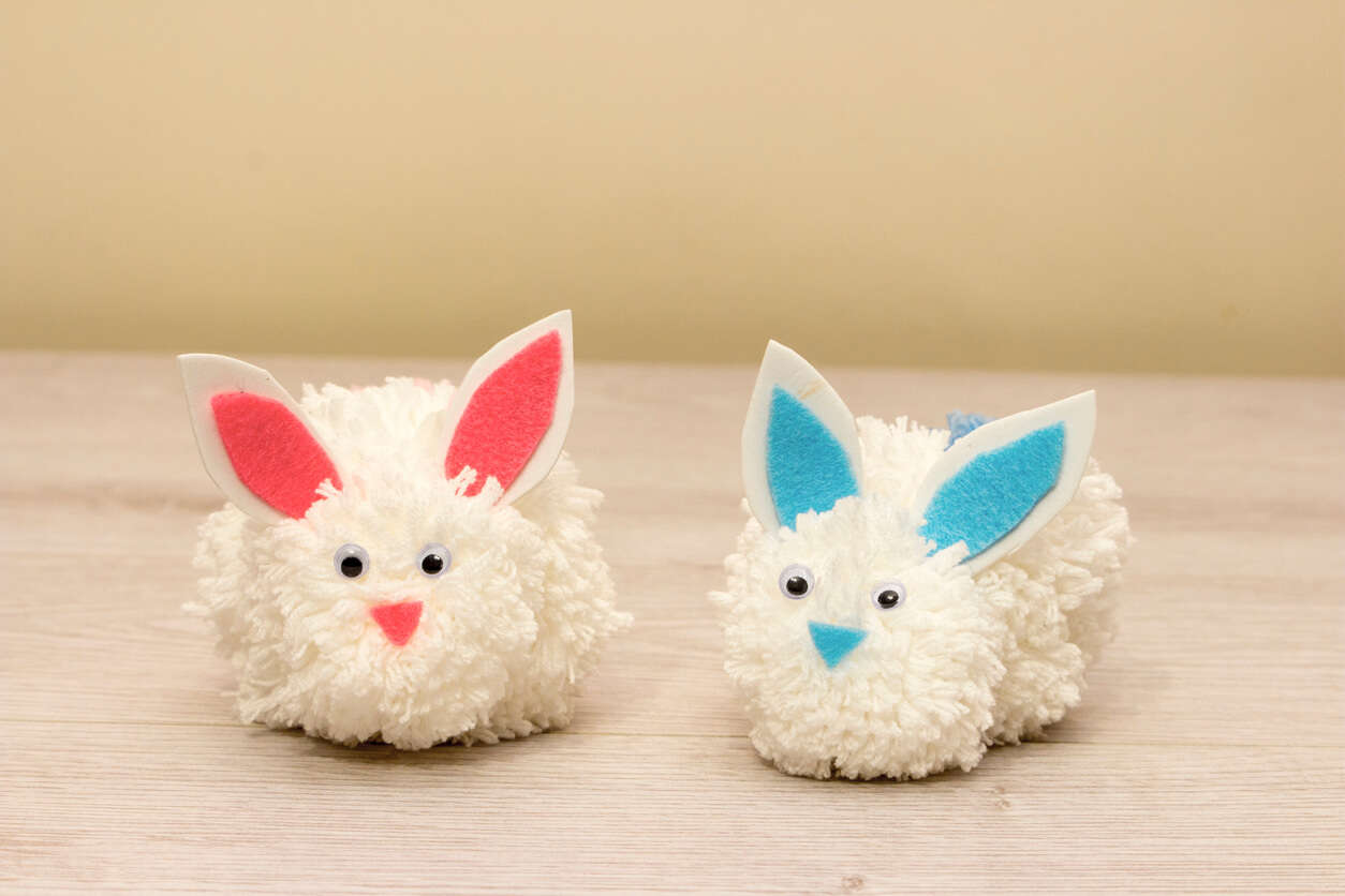 white pompom bunnies with blue and pink felt ears on a wooden table