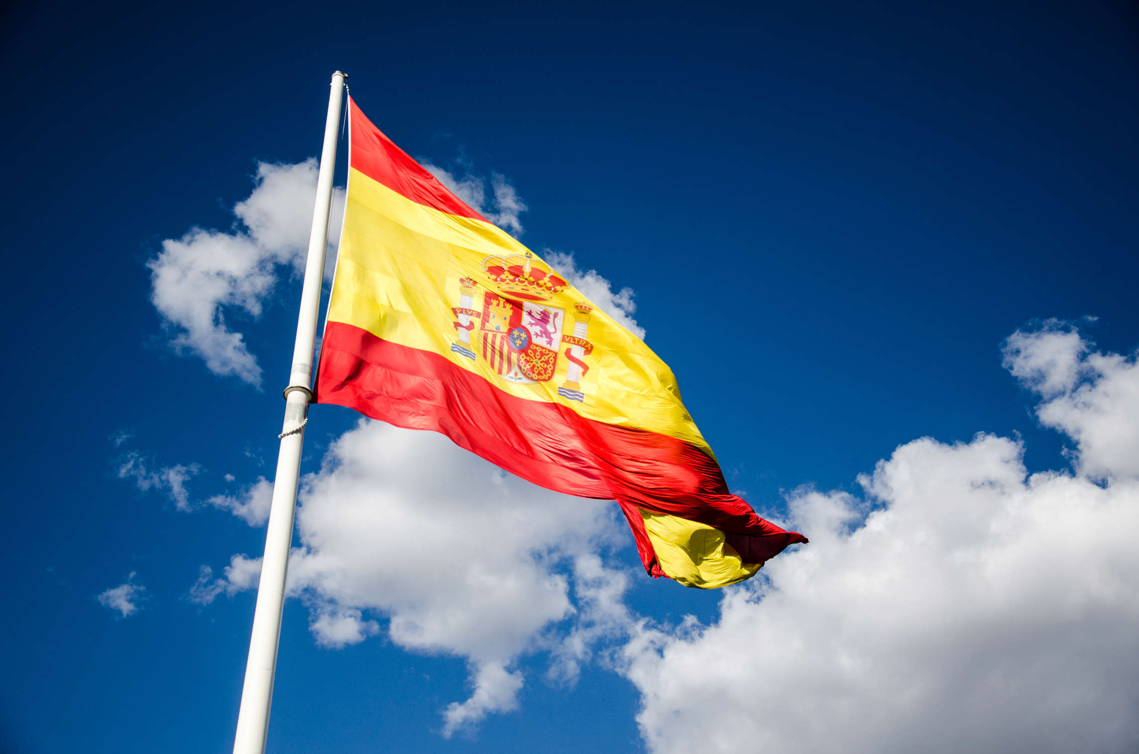 The Spanish flag on a blue sky with white clouds in the background
