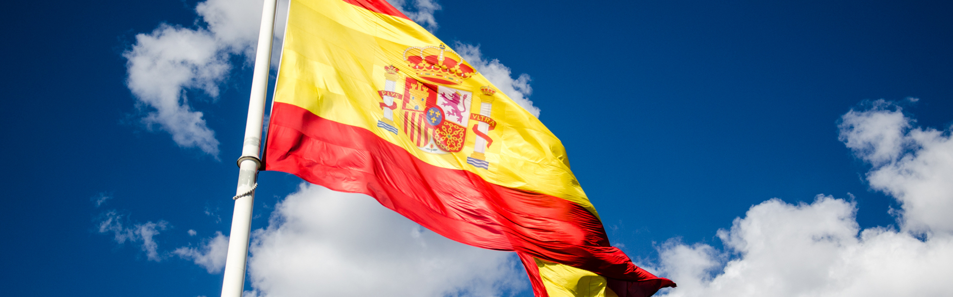 The Spanish flag on a blue sky with white clouds in the background