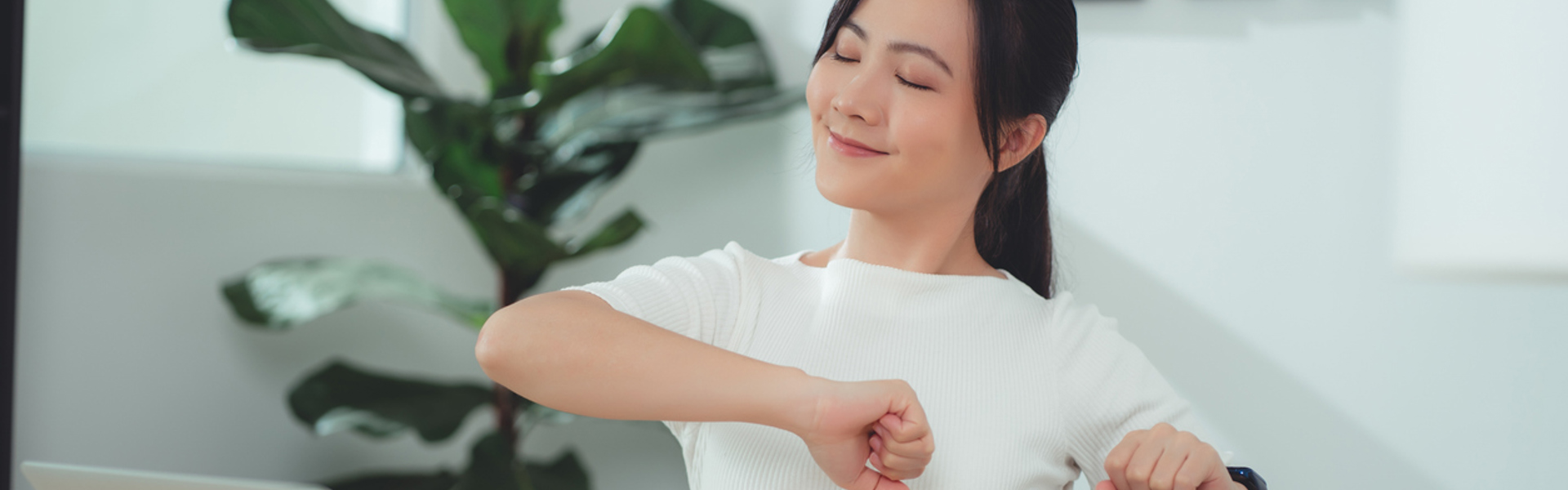 a woman sat at a work desk adjusting her posture and smiling