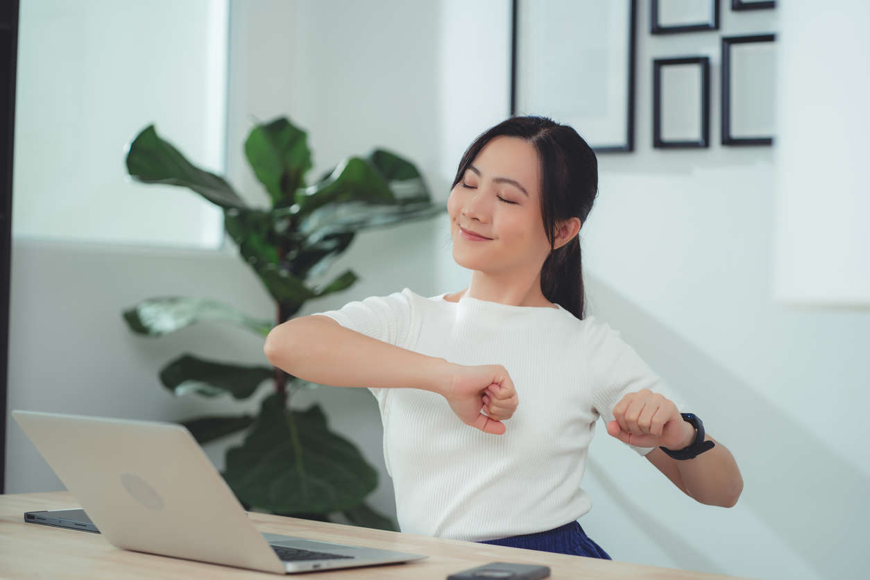 a woman sat at a work desk adjusting her posture and smiling