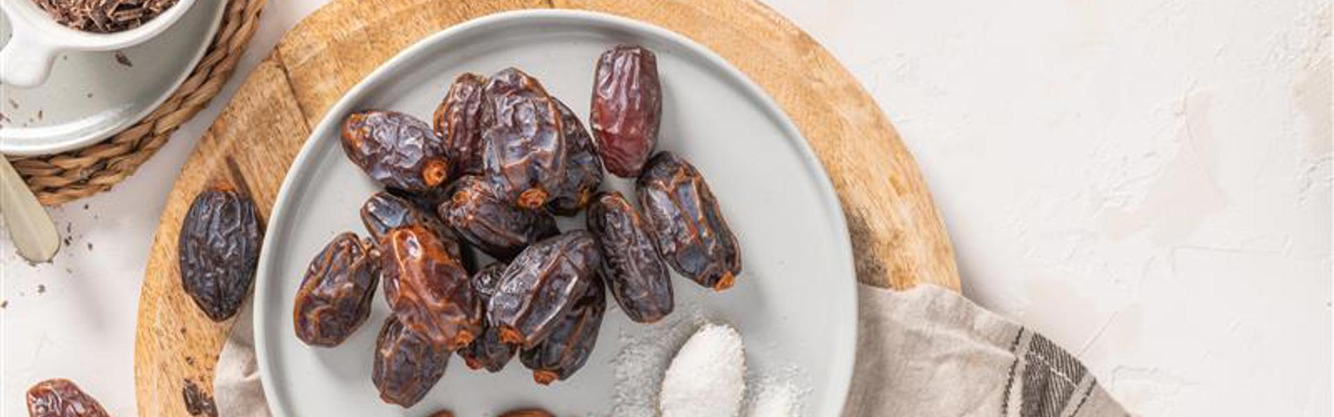 Main image: a bowl of dates with almonds and a spoon of sugar, ready to make almond stuffed dates to gift at Christmas.
