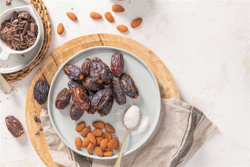 Main image: a bowl of dates with almonds and a spoon of sugar, ready to make almond stuffed dates to gift at Christmas.
