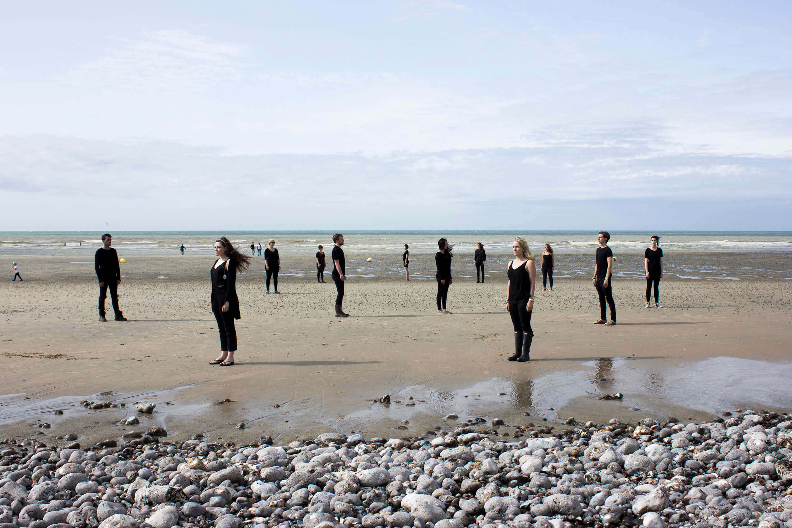 the London Contemporary Voices choir stood spaced out on a beach wearing black clothes